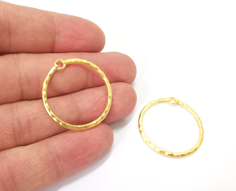 May include: Two gold-toned hammered metal hoops with a jump ring opening. The hoops are approximately 1 inch in diameter.