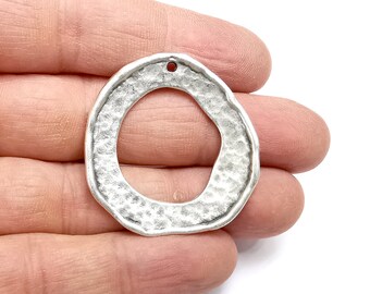 May include: Silver-toned metal pendant with a textured, irregular circular shape and a small hole at the top.