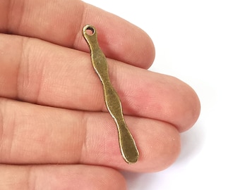 May include: A small, antique brass-colored metal charm with a wavy, elongated design. The charm has a small hole at the top for stringing and a rounded, paddle-like end. The charm is approximately 2 inches long.