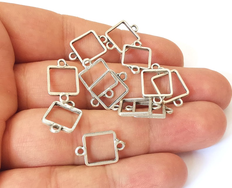 May include: A selection of silver-coloured square connector charms. Each charm has a hollow square design with small loops on each side for attaching to other components. These jewellery findings are ideal for crafting necklaces, bracelets, and earrings.
