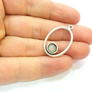 May include: Silver oval pendant with a smaller circle inside. The circle has a textured, white surface.