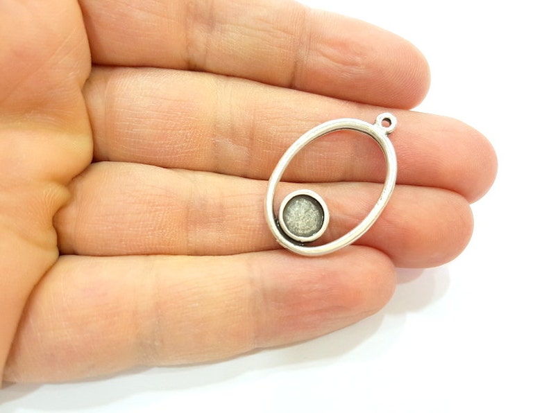 May include: Silver oval pendant with a smaller circle inside. The circle has a textured, white surface.