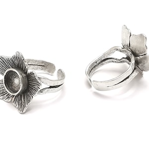 May include: Two silver adjustable rings with a flower design. Each ring has a round, open space in the center of the flower.
