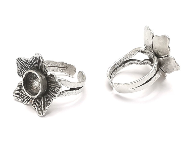 Op de afbeelding: Twee verstelbare zilveren ringen met een bloemmotief. Elke ring heeft een ronde, open ruimte in het midden van de bloem.
