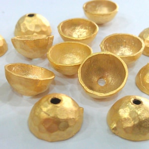 May include: A collection of 12 gold-toned metal dome-shaped beads with a hammered texture. The beads have a hole in the center for stringing.