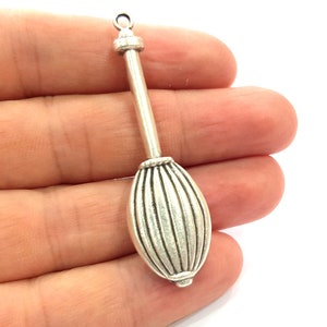 May include: Silver charm in the shape of a tambourine with a long handle. The charm has a detailed design with vertical lines on the tambourine part.