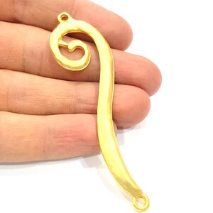 May include: Gold-toned metal pendant with a swirl design and two jump rings. The pendant is shaped like a curved line with a spiral at the top.