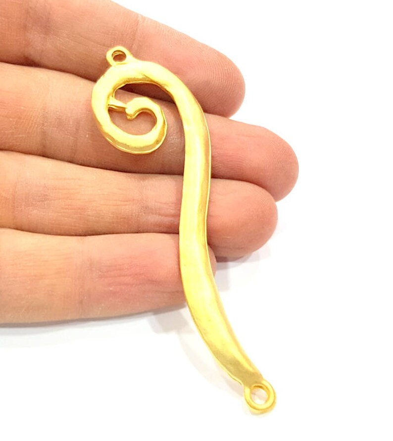 May include: Gold-toned metal pendant with a swirl design and two jump rings. The pendant is shaped like a curved line with a spiral at the top.