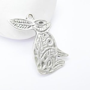 May include: Silver charm in the shape of a rabbit with intricate details. The rabbit is sitting upright with its ears raised.