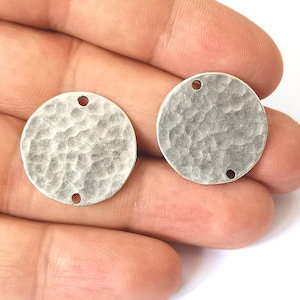 May include: Two silver-coloured, hammered-texture metal disc charms. Each charm is round with a slightly irregular surface and two small holes for attaching to jewellery. The charms are displayed against a neutral background.