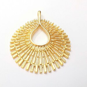 May include: A gold-toned pendant with a sunburst design. The pendant is made of metal and has a circular shape with a teardrop-shaped opening in the center.