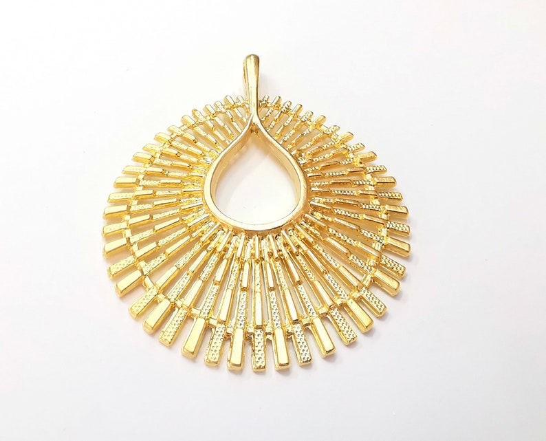 May include: A gold-toned pendant with a sunburst design. The pendant is made of metal and has a circular shape with a teardrop-shaped opening in the center.