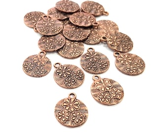 May include: A pile of 17 copper-colored metal charms with a floral design. The charms are round and have a hole at the top for attaching to jewelry or other crafts.