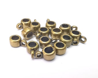 May include: A collection of small, antique brass-colored metal beads. Each bead has a cylindrical body with a dark interior and a small loop attached to the side. The beads are scattered on a white surface.
