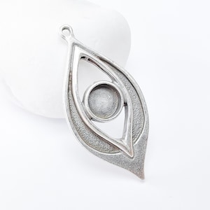 Può includere: Ciondolo in argento con un design a forma di occhio. Il ciondolo ha un'apertura rotonda per un cabochon.