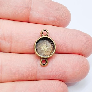 May include: An antique brass-coloured bezel connector. It has a round setting and two loops for attaching to other components. The setting is designed to hold a small cabochon. Suitable for jewellery making.