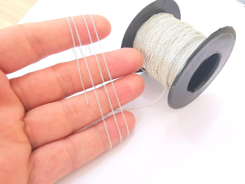 May include: A spool of silver chain, with several strands of the chain laid out on a hand.
