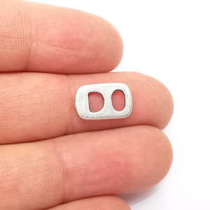 Puede incluir: Conector metálico plateado con dos agujeros ovalados. El conector es rectangular.