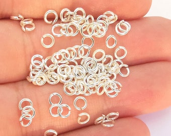 Op de afbeelding: Een grote stapel zilveren springringen, perfect voor het maken van sieraden. De ringen zijn klein en delicaat en liggen verspreid op een hand.