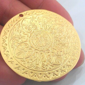 Peut inclure: Un pendentif en m&eacute;tal dor&eacute; avec un motif circulaire complexe. Le pendentif a un trou en haut pour l'accrocher.