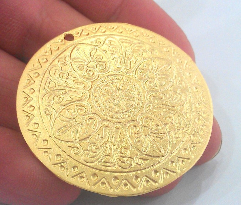 Peut inclure: Un pendentif en m&eacute;tal dor&eacute; avec un motif circulaire complexe. Le pendentif a un trou en haut pour l'accrocher.