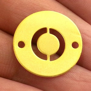 Peut inclure: Un cercle en métal de couleur dorée avec un motif découpé au centre. Le cercle a deux petits trous sur le bord.