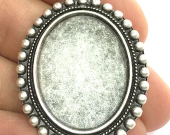 May include: Silver oval pendant with a beaded border and a loop at the top for hanging.