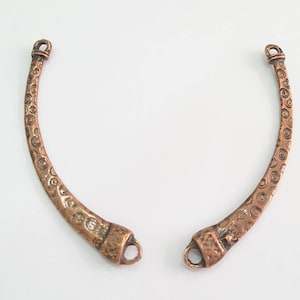 Puede incluir: Dos componentes de joyería de metal de color cobre, curvados. Cada pieza tiene una superficie texturizada con un patrón de remolino repetido y un lazo en cada extremo. Para la fabricación de joyas.