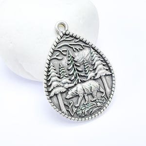 May include: Silver charm pendant featuring a detailed design of a bear walking through a forest with trees and foliage.