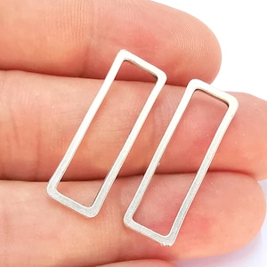 May include: Two silver metal rectangular jump rings. The rings are open and have a smooth, polished finish.