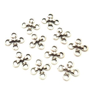 Op de afbeelding: Tien zilverkleurige metalen bloemvormige connector charms met elk vier lussen. De charms zijn perfect om een ​​toets van elegantie toe te voegen aan je sieradenmaakprojecten.