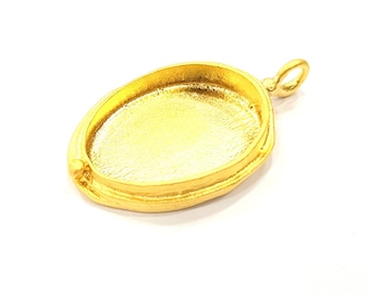 May include: A gold-colored pendant base with an oval shape and a small loop at the top. The pendant has a textured surface and a recessed area for setting a stone or other embellishment. The overall design is simple and elegant.