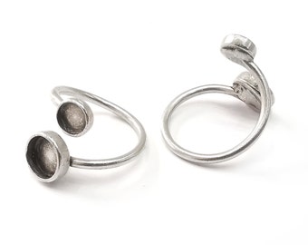 Könnte beinhalten: Zwei silberne Ringe mit runden, offenen Fassungen. Die Ringe sind so konzipiert, dass sie am Finger getragen werden, wobei die Fassungen nach oben zeigen.