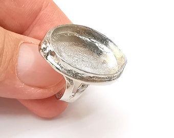 May include: A silver-colored ring with an oval bezel setting. The ring has a textured band and a raised bezel to hold a stone or other embellishment. The ring is designed for jewelry making and crafting.