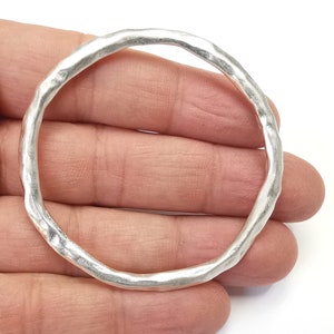 May include: A silver bangle bracelet with a hammered texture. The bracelet is thick and has a rounded shape.