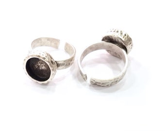 May include: Two silver adjustable rings with a round bezel setting for a cabochon stone. The rings have a hammered texture.
