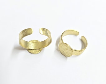Może przedstawiać: Dwa regulowane pierścionki w kolorze złotym z młotkowaną fakturą. Każdy pierścionek posiada okrągły, płaski element centralny. Pierścionki są prezentowane na białej powierzchni, prezentując swój prosty, ale elegancki design.