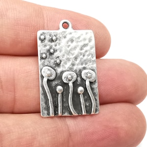 May include: Silver charm with a textured rectangular design featuring five stylized flower buds with rounded tops. The charm has a loop at the top for attaching to a necklace or bracelet.