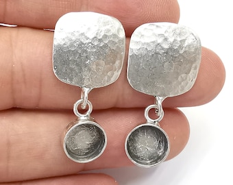 May include: A pair of silver earrings with a hammered square shape and a round pendant. The earrings are made of sterling silver and have a polished finish.