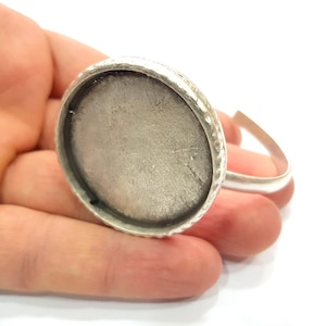 May include: Silver bracelet with a round, silver-toned bezel setting. The bezel is textured and has a slightly raised edge.