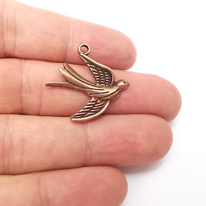 Pode incluir: Um amuleto de metal de cor cobre em forma de andorinha voando.