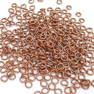 May include: A large pile of small, copper-colored jump rings. The rings are all the same size and are arranged in a random pattern.