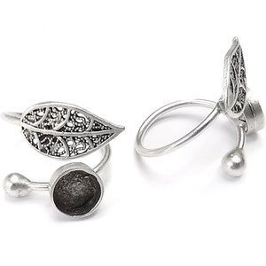 Op de afbeelding: Twee zilveren ringen in de vorm van een blad met een ronde bezel-setting. De ringen zijn open en kunnen worden aangepast aan verschillende vingermaten.