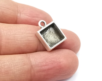 Puede incluir: Pendiente de plata con un bisel cuadrado para una pequeña pieza de joyería. El bisel está abierto en la parte posterior y tiene un bucle en la parte superior para sujetar una cadena.