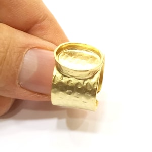 以下が含まれることがあります： カボションストーン用の丸いベゼルセッティングが付いたゴールドリング。リングバンドにはハンマードテクスチャが施されています。