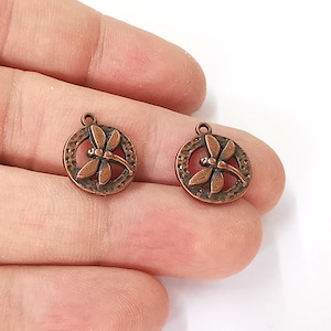May include: Two copper-colored metal charms featuring a dragonfly design. Each charm is round with a textured surface and a loop for attaching to jewelry or other crafts.