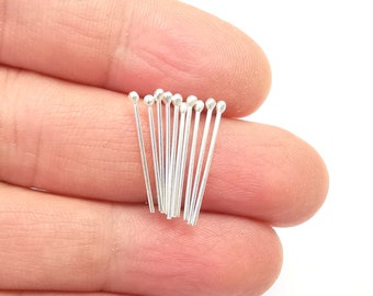 May include: A collection of small, thin, silver-colored metal headpins, each featuring a tiny spherical ball at one end. These straight, slender jewelry-making components are arranged in a parallel cluster, showcasing their metallic finish.