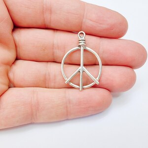 May include: Silver peace sign charm pendant. The charm is a simple, open circle design with a peace sign inside. The charm is perfect for adding a touch of peace and love to any jewelry project.