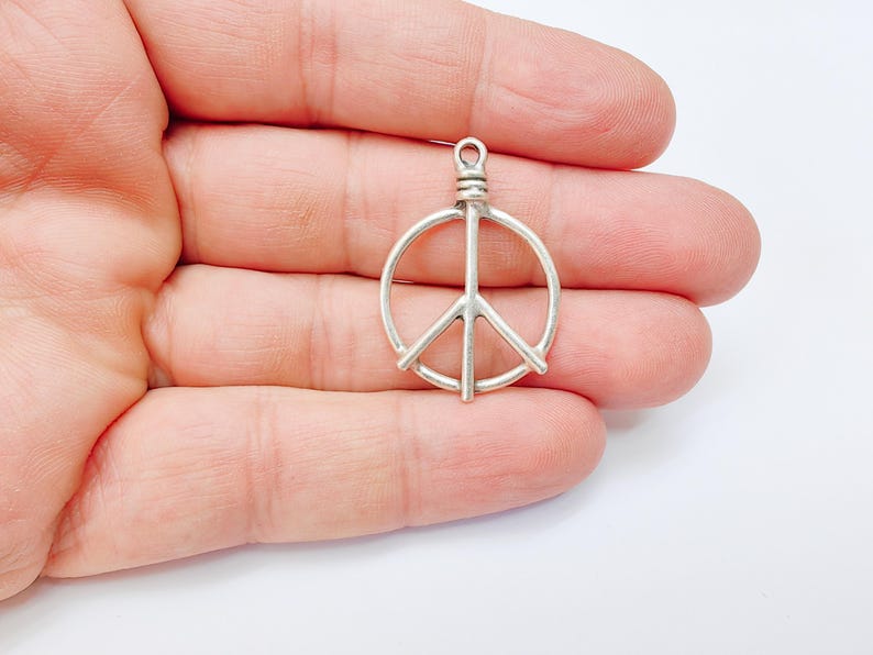 May include: Silver peace sign charm pendant. The charm is a simple, open circle design with a peace sign inside. The charm is perfect for adding a touch of peace and love to any jewelry project.
