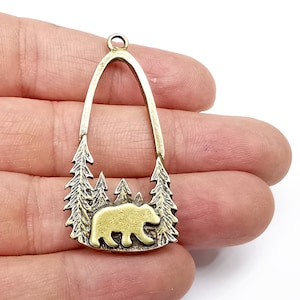 May include: A gold-toned metal pendant shaped like an archway with a bear silhouette inside. The archway is decorated with pine trees on either side.